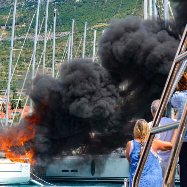 A group of people looking at a boat on fire

Description automatically generated with medium confidence